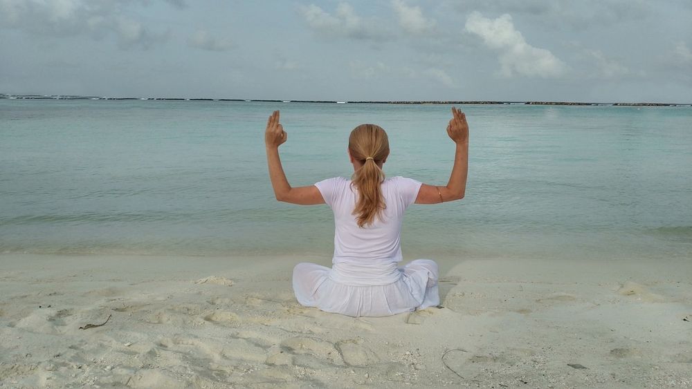 Mari Carmen Adsuara sentada en la orilla del mar, practicando yoga
